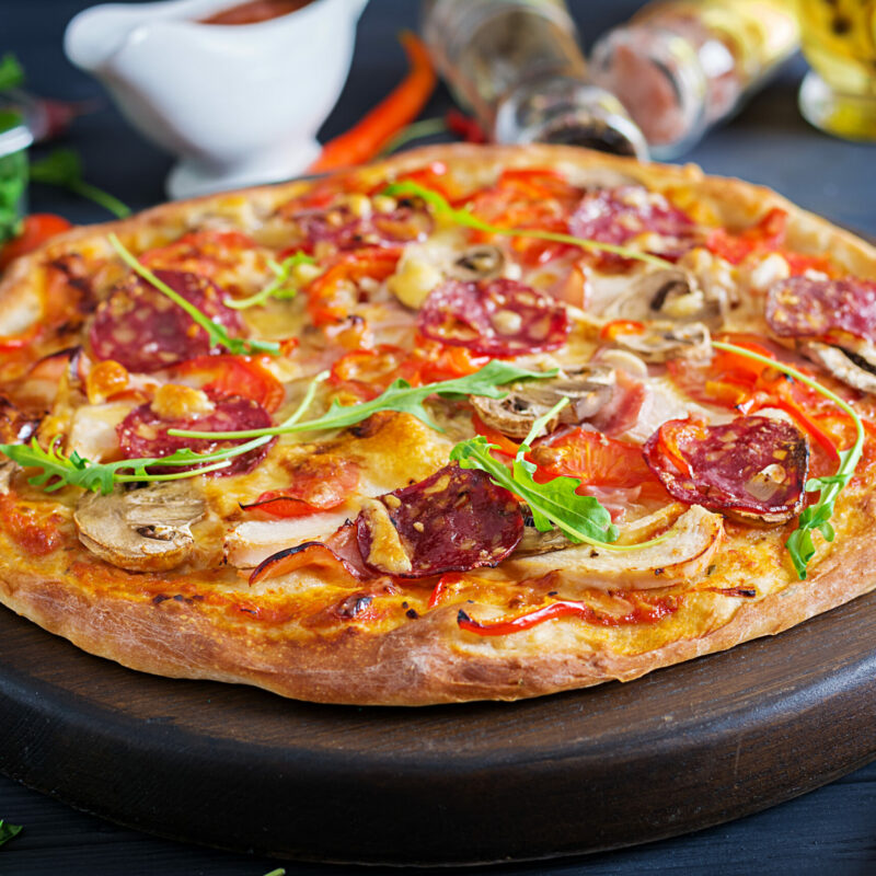 Fresh Italian pizza with chicken fillet, mushrooms, ham, salami, tomatoes, cheese on a black background. Italian food.